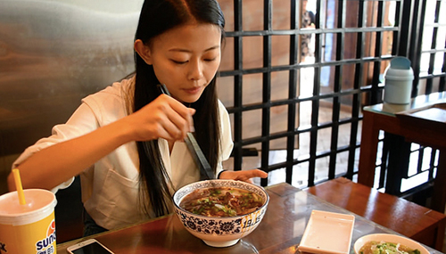 Young Chinse girl eating beef noodle soup at noodle soup shop in Lanzhou